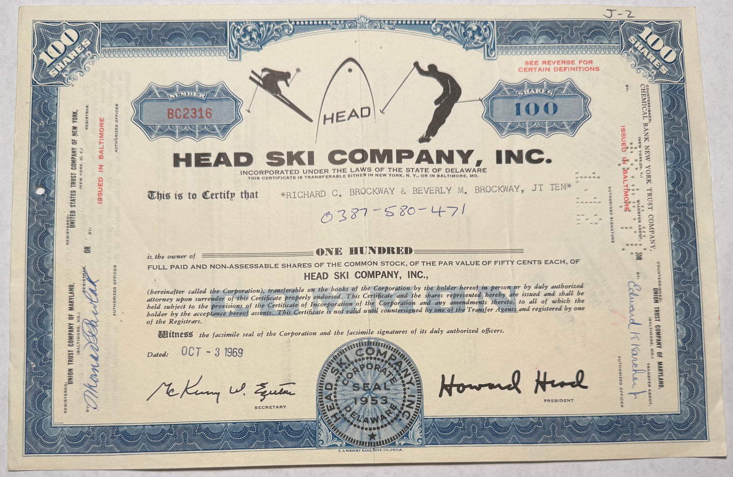 Blue stock certificate with cancellation holes, writing and stamps present. Dated 1969